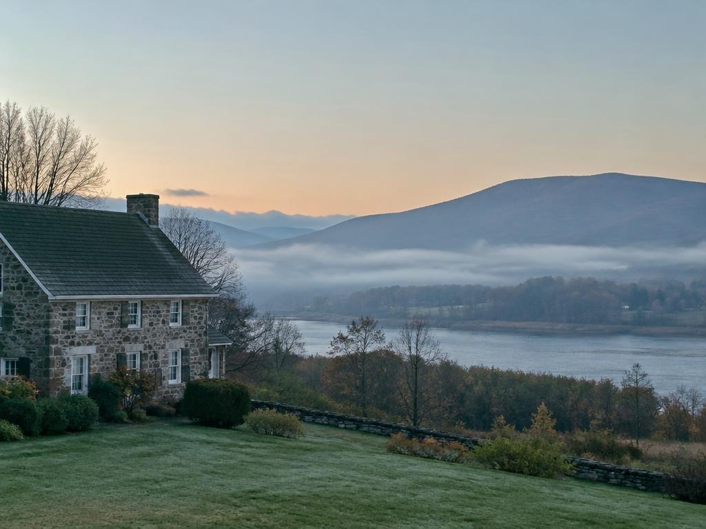 Illustrative image: a stone farmhouse above a misty river valley at dawn
